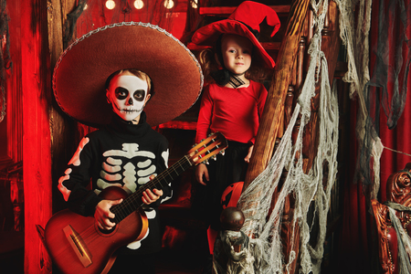 Two funny kids in carnival costumes in an old wooden house with pumpkins. Dia de los muertos. Day of The Dead. Halloween.の写真素材