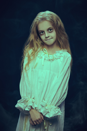 Portrait of a scary little girl ghost in a white nightgown. Black background. Halloween.の写真素材