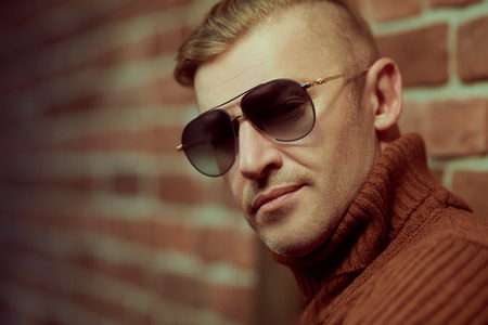Handsome mature man in sunglasses over brick wall background. Optics style.の写真素材