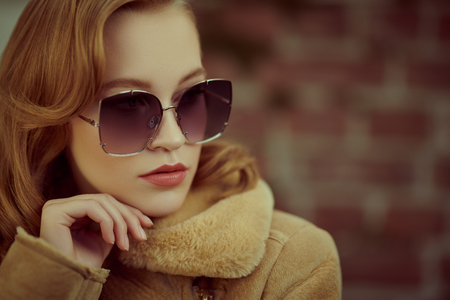 Close-up portrait of a fashionable young woman in modern sunglasses over brick wall backgroud. Winter style. Beauty, fashion concept. Optics, eyewear. Copy space.の写真素材
