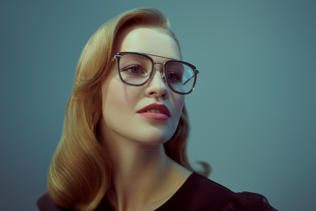Studio portrait of a beauty fashion blonde model girl wearing stylish glasses. Elegant young woman with natural makeup and trendy accessories. Optics style, eyewear.の写真素材