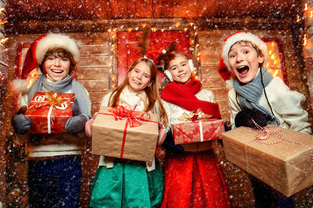 Four happy children stand with gifts near the house decorated for Christmas. Merry Christmas and Happy New Year. Winter holidays concept.の写真素材
