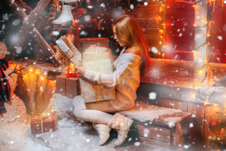 Pretty child girl sits on the porch of a house decorated for Christmas and opens a gift box and surprises. Time for miracles.の写真素材