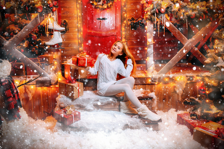 Pretty child girl is sitting  and is holding  a gift box on the porch of a house decorated for Christmas. Time for miracles.の写真素材