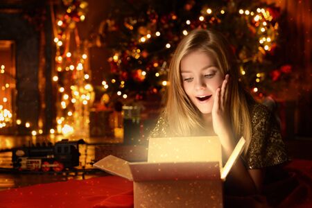 Pretty nine year old girl opens a gift box and surprises. Luxurious apartments decorated for Christmas. Merry Christmas and Happy New Year.の写真素材