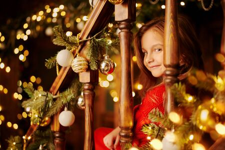 Happy little girl celebrates Christmas in a house beautifully decorated with spruce garlands and New Year's toys. The atmosphere of magic, lights and sparkle is around.の写真素材