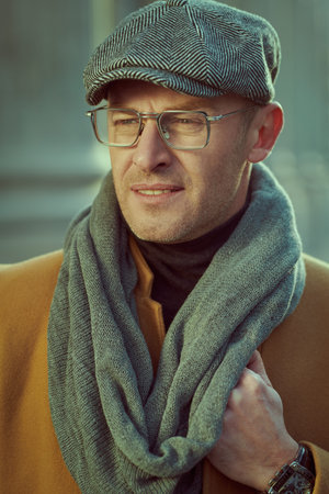 Portrait of a handsome mature man in elegant clothes and glasses walking on a city street. Fashion...