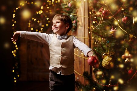 Happy little boy in elegant festive suit decorates beautiful Christmas tree at home. Merry Christmas and Happy New Year!の写真素材