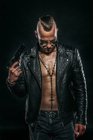 Dark portrait of a serious gangster man with gun wearing black leather jacket.の写真素材