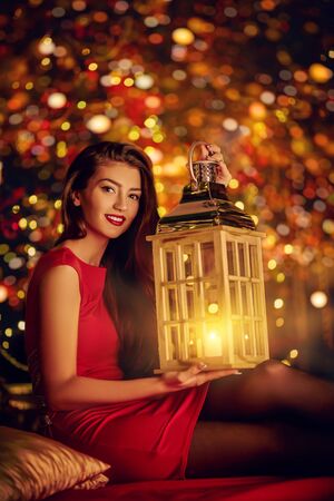 Christmas and New Year concept. Beautiful happy girl celebrates Christmas in the fairy Christmas interior with lights around. Christmas tree in the background.の写真素材