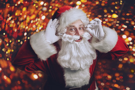 Magical Christmas time. Jolly Santa Claus looking into the camera and surprised. Magic golden lights...