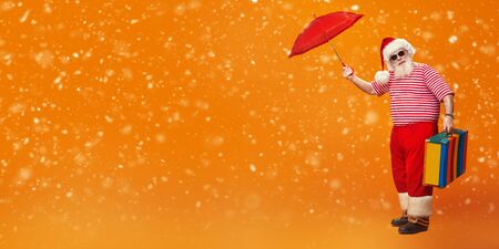 Jolly funny Santa Claus goes on vacation. Christmas Holidays, tourist trips to hot tropical countries. Bright yellow background. Copy space.の写真素材