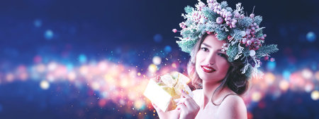 Christmas winter beauty woman. Charming girl with Christmas decoration on her head holds a gift box...