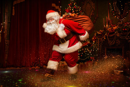 Santa Claus is getting out of the fireplace with a bag of gifts. Beautiful Christmas interior....