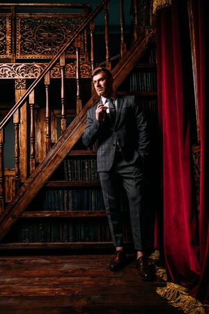 A portrait of a handsome mature man in a formal costume posing near the stairs and a bookcase. Men's beauty, fashion.の写真素材