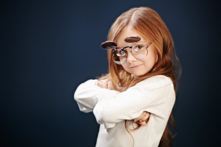 Portrait of a funny little girl in glasses on a dark background. Fashion trends for kids.