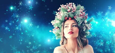 Christmas magic. Beautiful young woman with a Christmas spruce wreath on her head on snow background.の写真素材