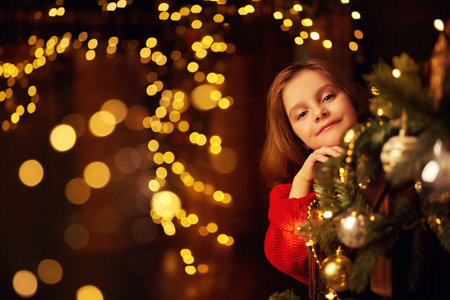 Merry Christmas and Happy New Year! Happy little girl celebrates Christmas in a house beautifully decorated with spruce garlands and New Year's toys. The atmosphere of magic, lights and sparkle is around.の写真素材