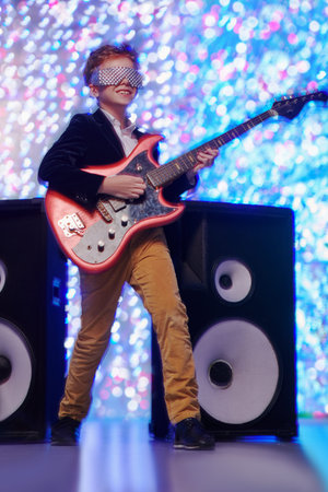 Christmas and New Year kid's party. Cool modern boy sings and plays electric guitar next to the speakers. Disco and lights.の写真素材