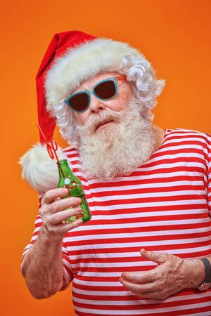 Santa Claus in a red hat and sunglasses holding a bottle of drink on a yellow background. Christmas Holidays, tourist trips to the sea. Bright yellow background.の写真素材