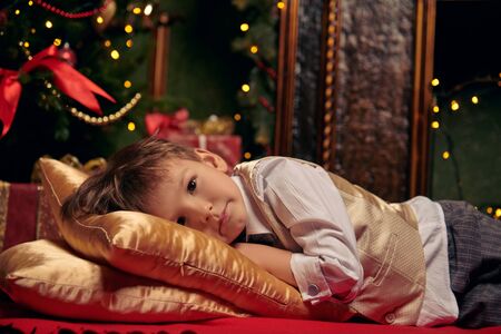 Cute little boy lying on pillows on the floor in a cozy atmosphere near a beautiful New Year. Magic for Christmas.の写真素材