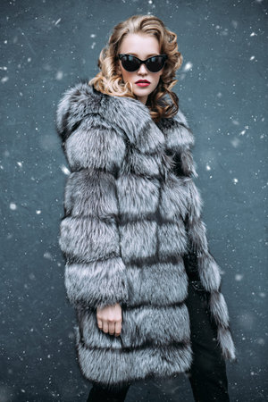 Stylized red portrait of a beautiful woman wearing a fur coat with hood and sunglasses. Beauty,...