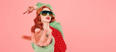 Portrait of a fashionable young woman posing in a red dress and a fur coat. Fashion shot over pink background. Copy space.の写真素材