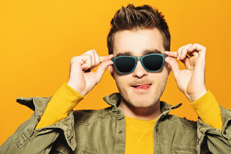 A portrait of a fashionable young man posing in the studio over the yellow background. Casual...