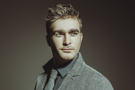 A portrait of a fashionable young man posing in the studio over the grey background. Formal fashion...