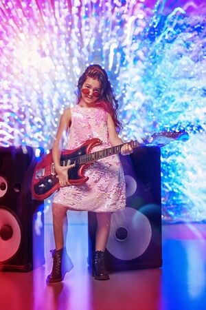 Christmas and New Year kid's party. Cool little girl sings and dances with an electric guitar next to the speakers. Disco and lights.の写真素材