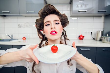 Diet and weight loss concept. Young expressive pretty woman is going to eat cherry tomato. Pin-up style.の写真素材