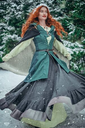 Beautiful young woman in medieval clothes is walking in a winter forest. Historical reconstruction of the early Middle Ages. Christmas tale.の写真素材