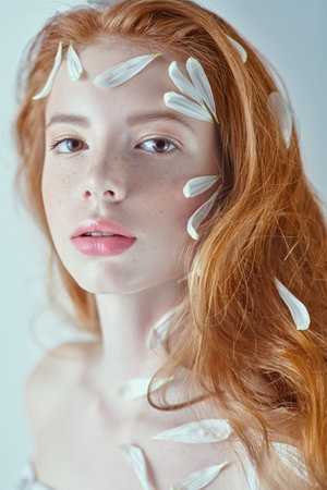 Portrait of a beautiful tender girl with white chrysanthemum petals on her face and body on a white background. Beauty, spa and cosmetics concept.の写真素材