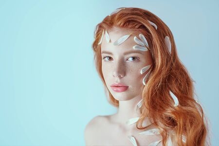 Portrait of a beautiful tender girl with white chrysanthemum petals on her face and body on a white background. Beauty, spa and cosmetics concept. Copy space.の写真素材