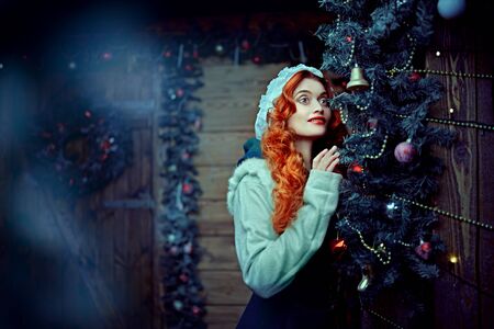 Christmas fairy tale. Beautiful happy young woman with magnificent red hair in a wooden house decorated on Christmas.の写真素材
