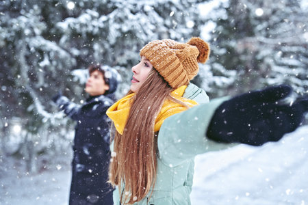 Happy girl and young man are standing in a beautiful winter park, they spread their arms to the...