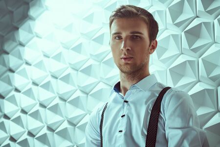 Men's fashion. Portrait of a handsome sensual young man in a formal suit by a white tech background. Businessman portrait.の写真素材