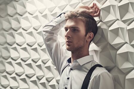 Men's fashion. Portrait of a handsome sensual young man in a formal suit by a white tech background. Businessman portrait.の写真素材