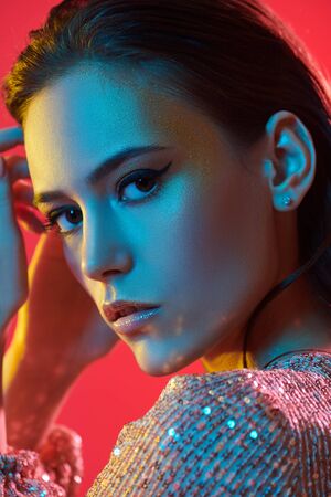 Make-up and cosmetics. Portrait of a gorgeous young woman with golden make-up in a colored red, blue and yellow light. Party style.の写真素材
