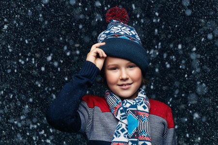 Portrait of a cute emotional boy child in winter clothes under the snow. Kid's fashion. Winter...