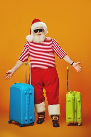 Jolly Santa Claus goes on vacation to the sea. Christmas Holidays, tourist trips to hot tropical countries. Bright yellow background. Copy space.の写真素材