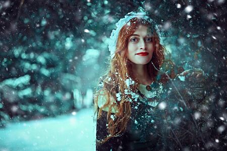 Portrait of a beautiful young woman with long red hair wearing medieval clothes walks through a winter snowy forest. Historical reconstruction of the early Middle Ages. Christmas tale.の写真素材