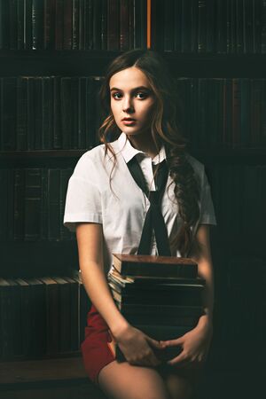 Beautiful girl wearing school uniform holding books in the old library. Beauty, fashion. Educational concept.の写真素材