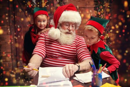 Santa Claus and little elves are sorting mail, reading letters from children. House, workshop of Santa Claus.の写真素材