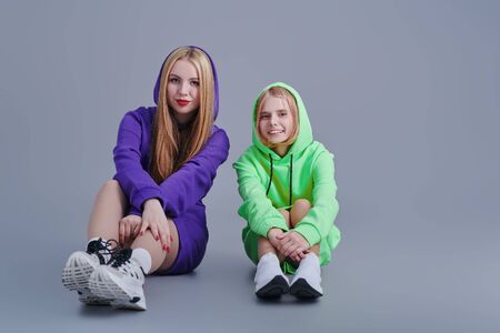 Two sisters in bright sweatshirts pose in the studio. Youth style and fashion.の写真素材