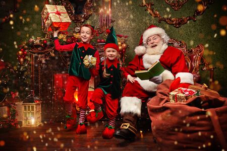 Jolly Santa Claus and his elves are preparing gifts for Christmas at home. Merry Christmas and Happy New Year!の写真素材