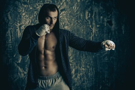 Handsome athletic man in hoodie stands by a grunge wall. Boxer, street fighter.の写真素材