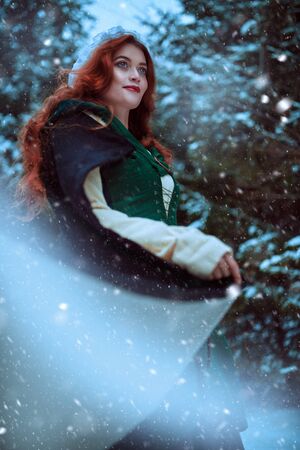 Beautiful young woman in medieval clothes is walking in a winter forest. Historical reconstruction of the early Middle Ages. Christmas tale.の写真素材