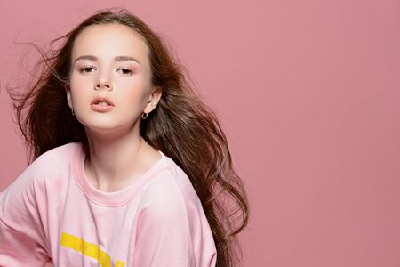 Teen style. Beautiful young model with long hair posing at studio in jeans and pink sweatshirt. Beauty, fashion.の写真素材