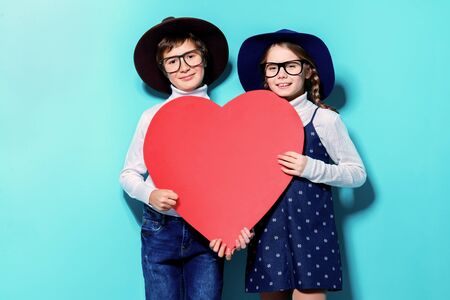 Happy pre-teen boy and girl holding big red heart over blue background. Friendship. First love. Valentine's Day.の写真素材